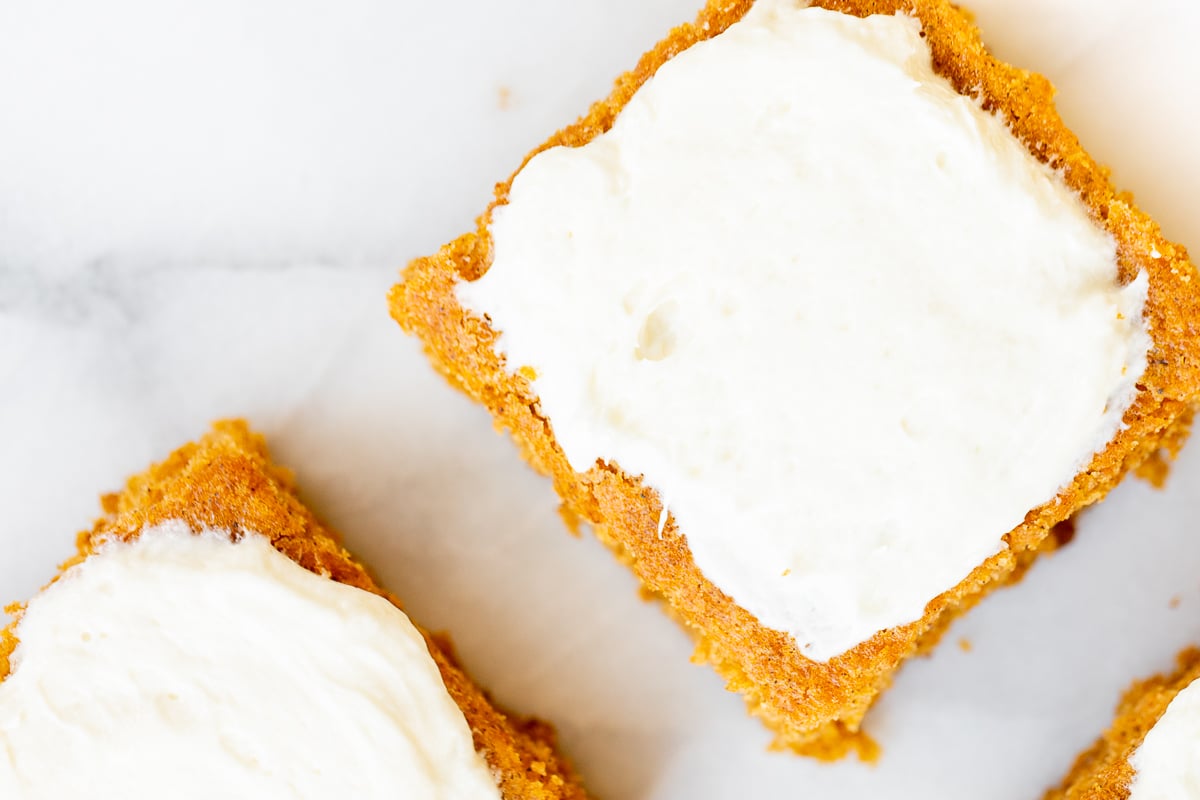 Pumpkin bars with cream cheese frosting on a marble surface.