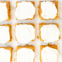 Pumpkin bars with cream cheese frosting on a marble surface.