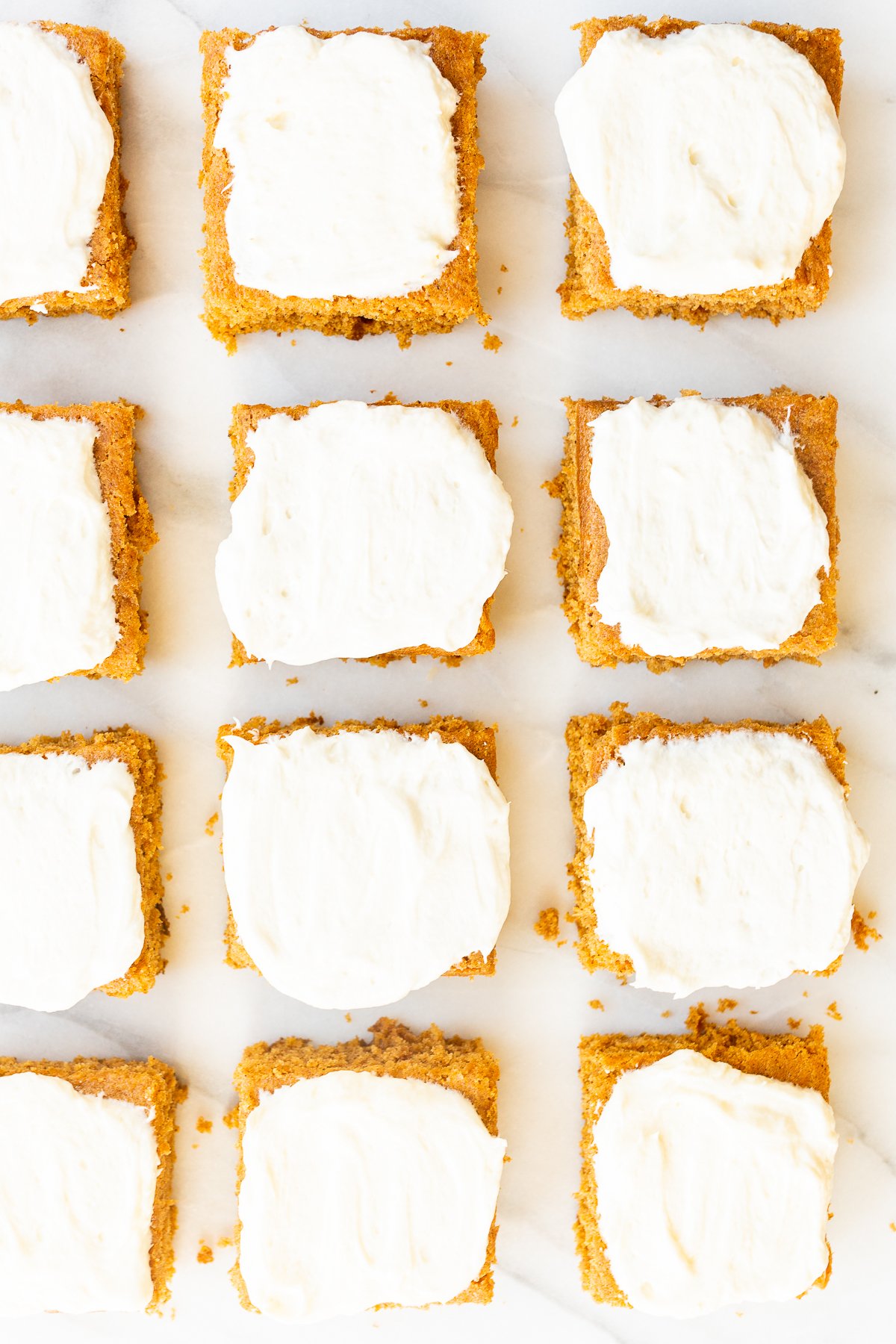 Pumpkin bars with cream cheese frosting on a marble surface. 