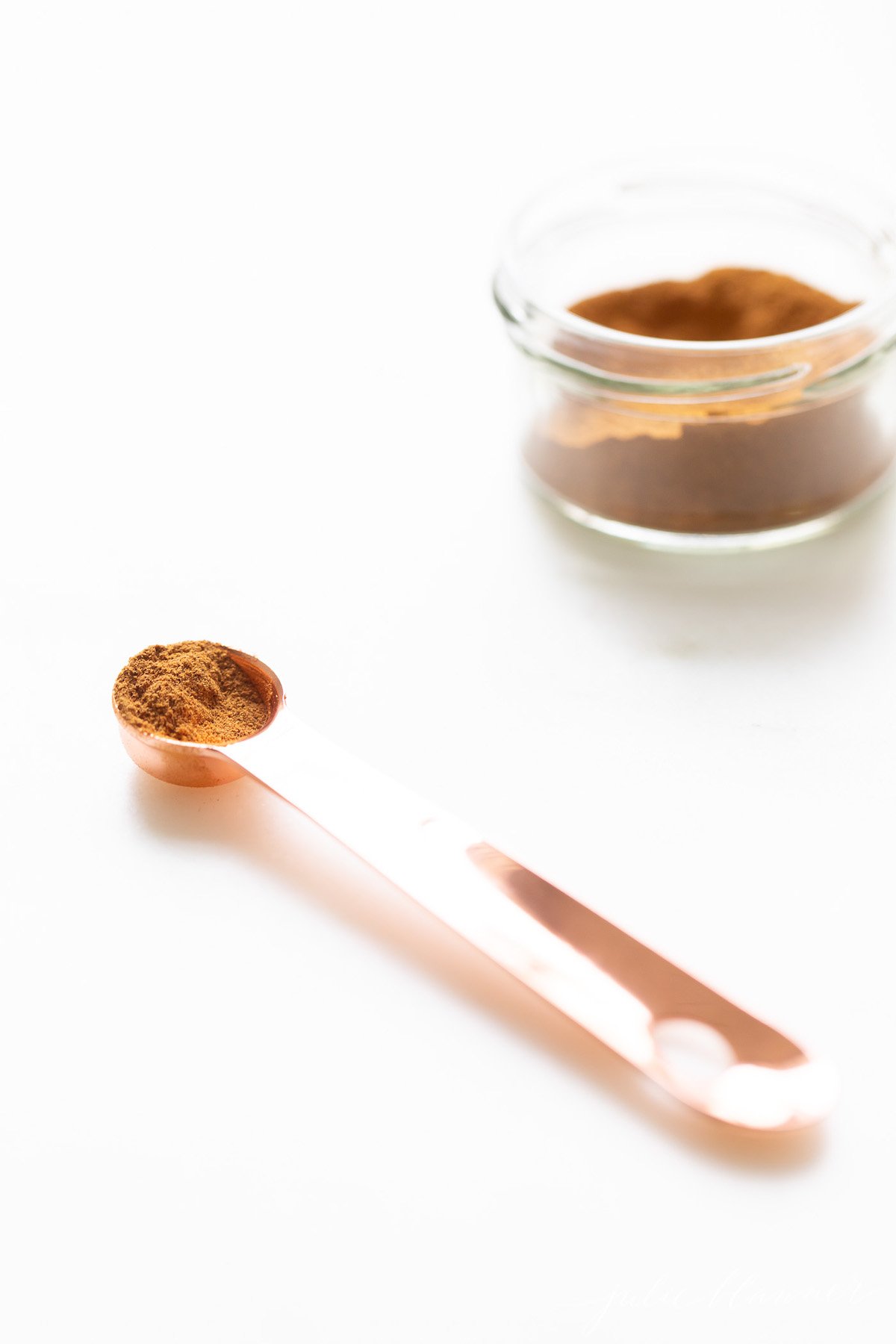 A small clear jar of pumpkin pie spice on a white countertop.