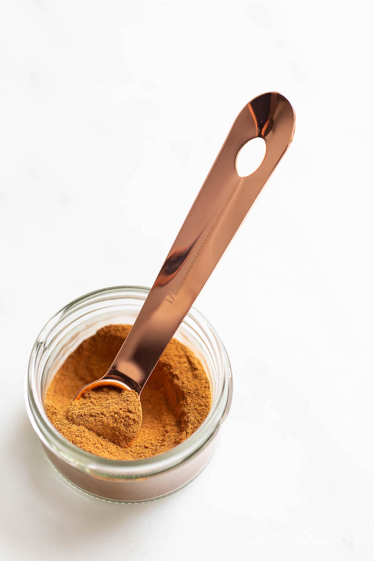 A small clear jar of pumpkin pie spice on a white countertop.