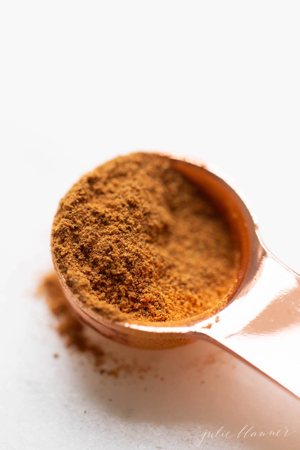 A copper teaspoon full of homemade pumpkin pie spice on a white countertop.