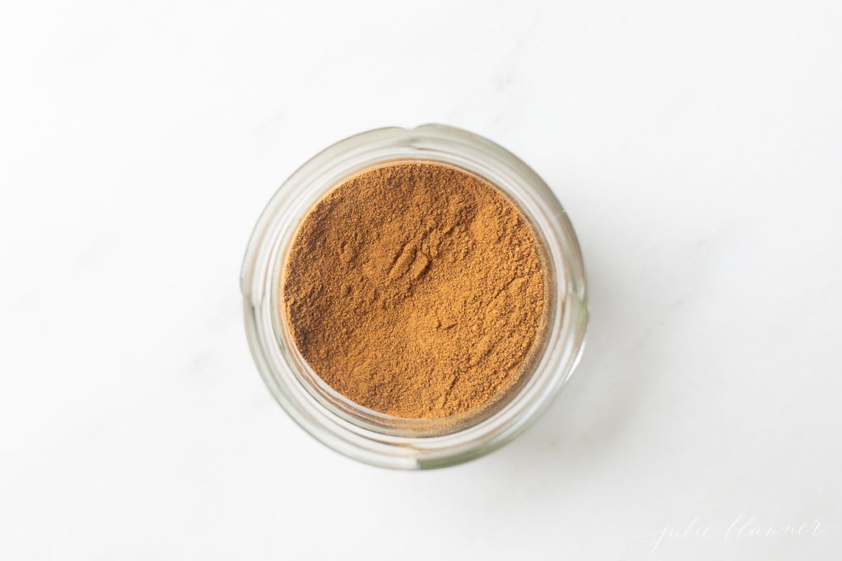 A small clear jar of pumpkin pie spice on a white countertop.