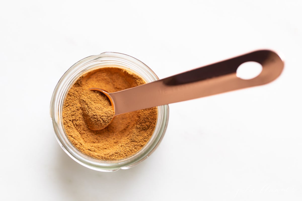 A small clear jar of pumpkin pie spice on a white countertop.