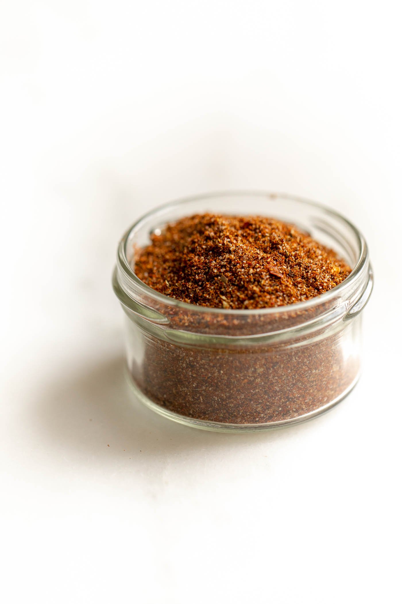 A small glass jar full of taco seasoning on a marble countertop.