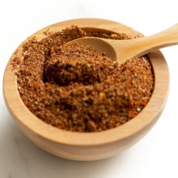 A small wooden bowl full of homemade taco seasoning, with a wooden teaspoon inside.