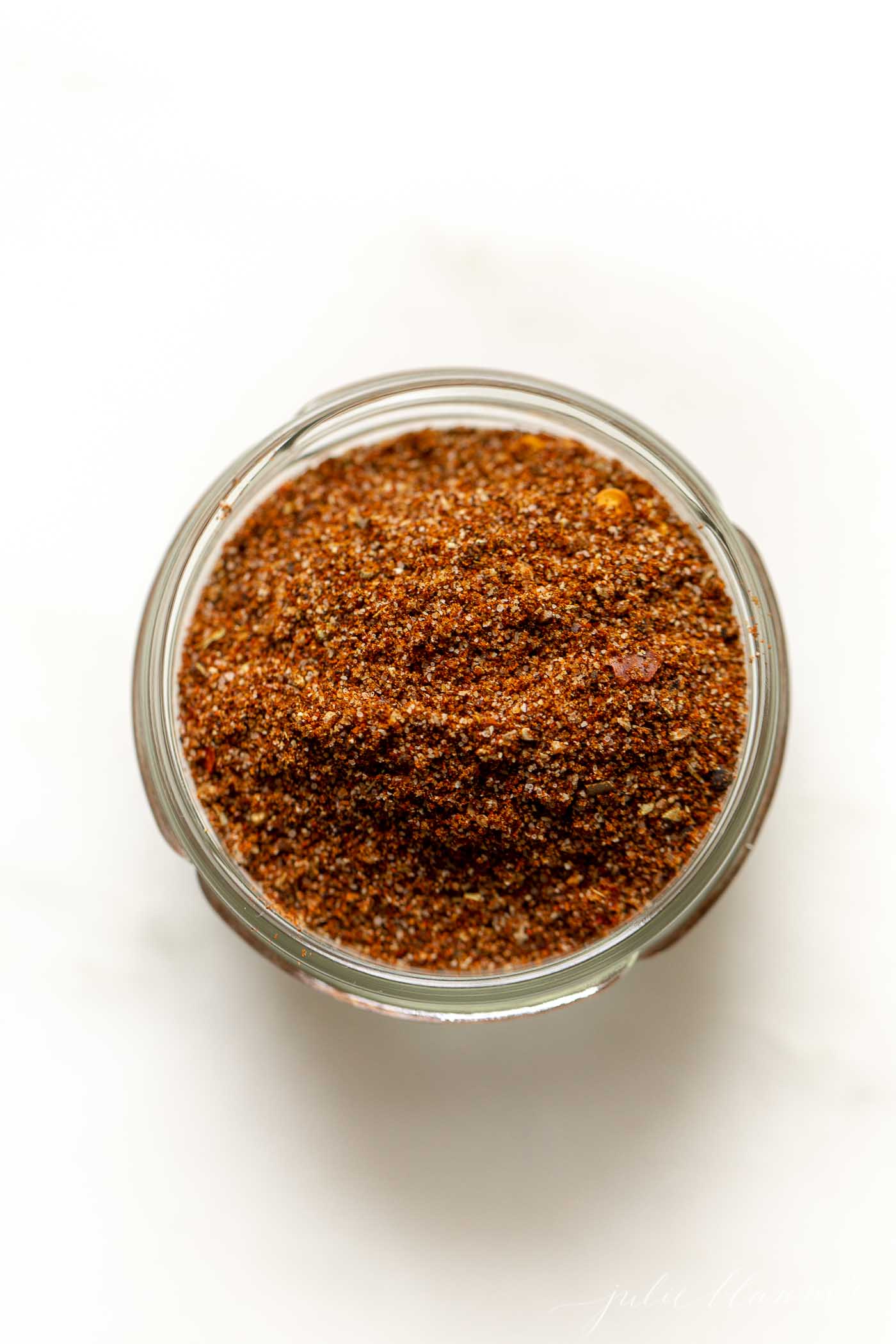 A small glass jar full of taco seasoning on a marble countertop.