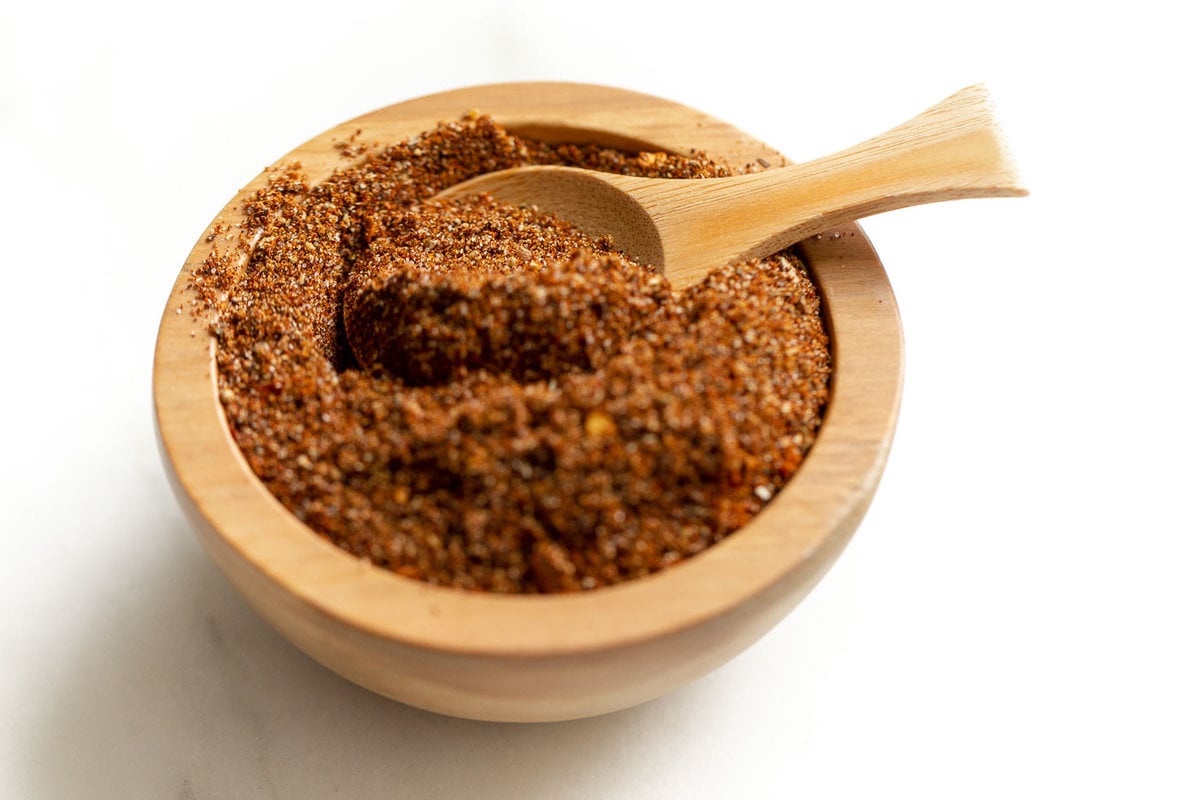 A small wooden bowl full of homemade taco seasoning, with a wooden teaspoon inside.