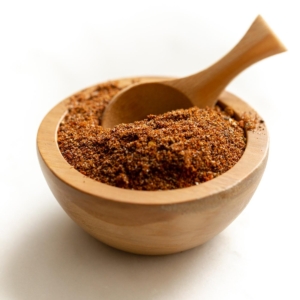 A small wooden bowl full of homemade taco seasoning, with a wooden teaspoon inside.