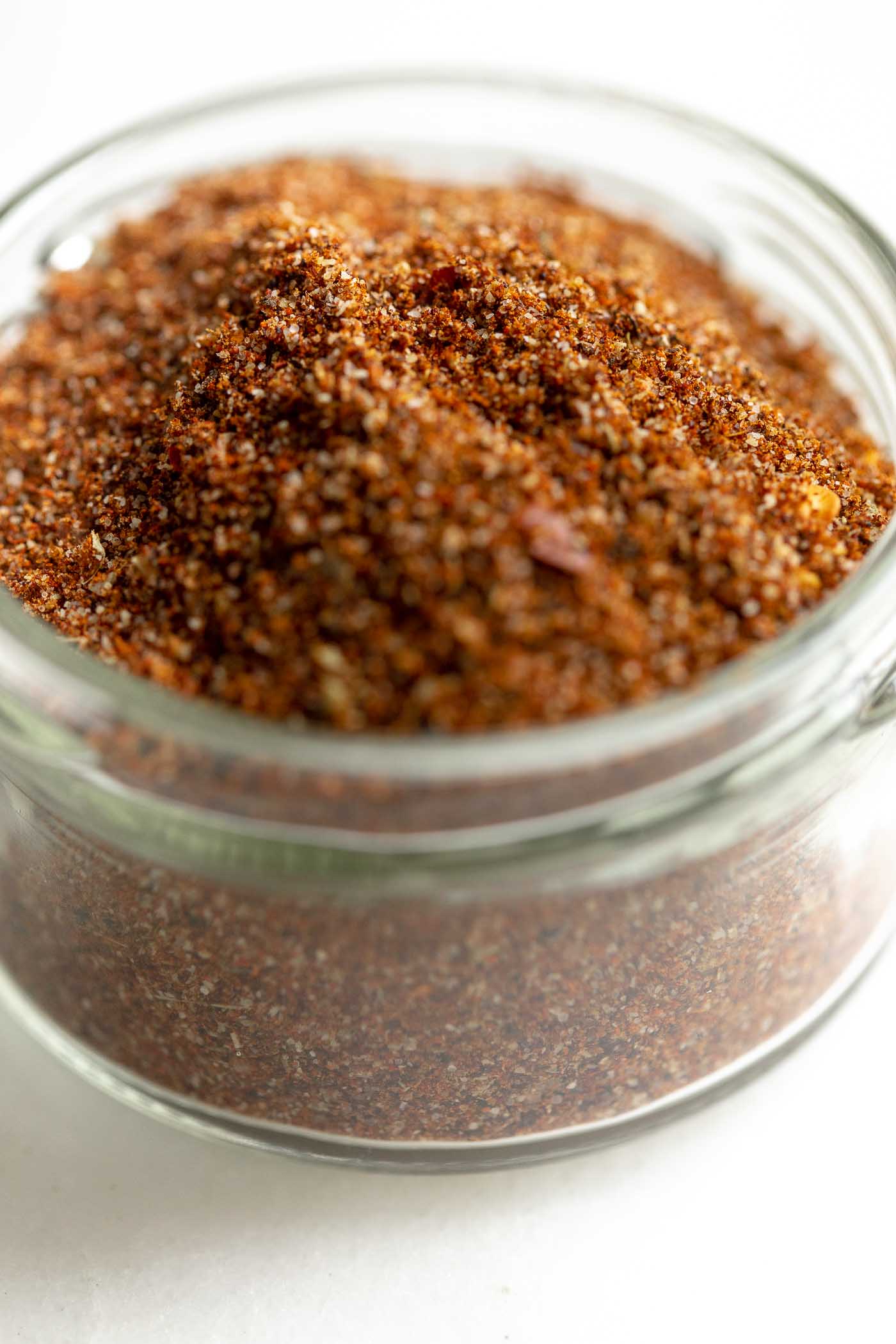 A small glass jar full of taco seasoning on a marble countertop.