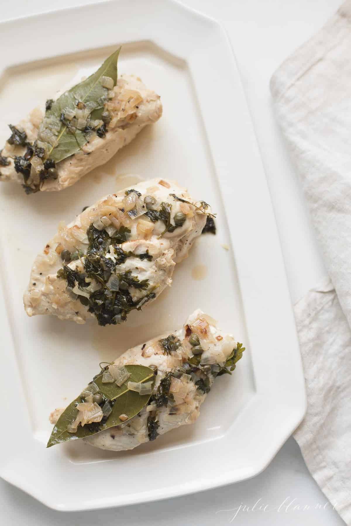 3 baked chicken breasts covered in herbs on a white platter.