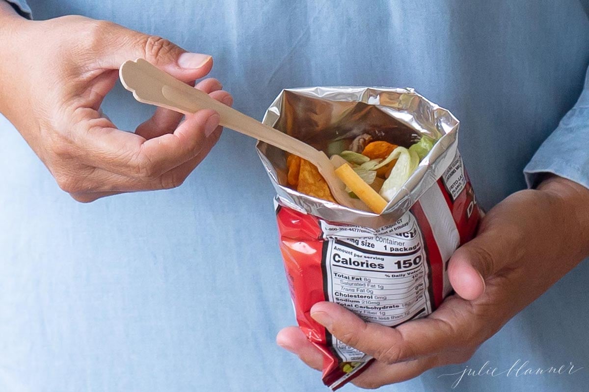 A woman enjoying a Doritos bag of a walking tacos recipe with sour cream and guacamole.