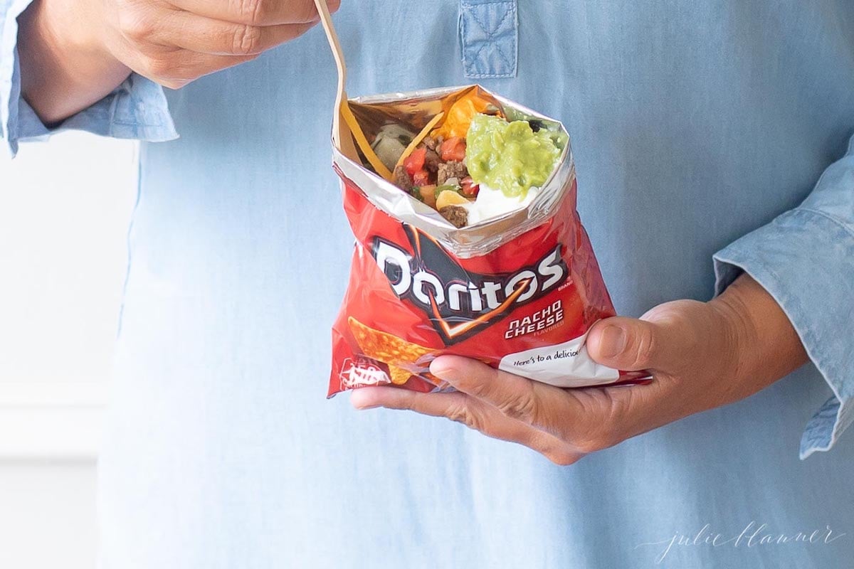 A woman enjoying a Doritos bag of a walking tacos recipe with sour cream and guacamole.