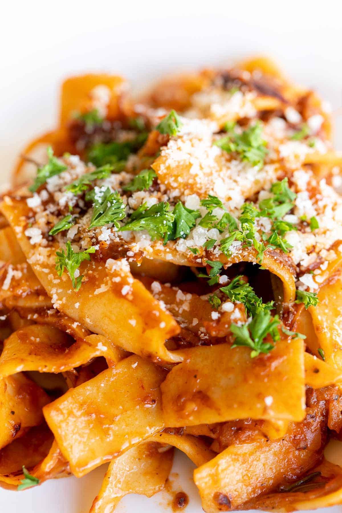 A close up of pappardalle pasta with beef ragu sauce, topped with parsley and parmesan.