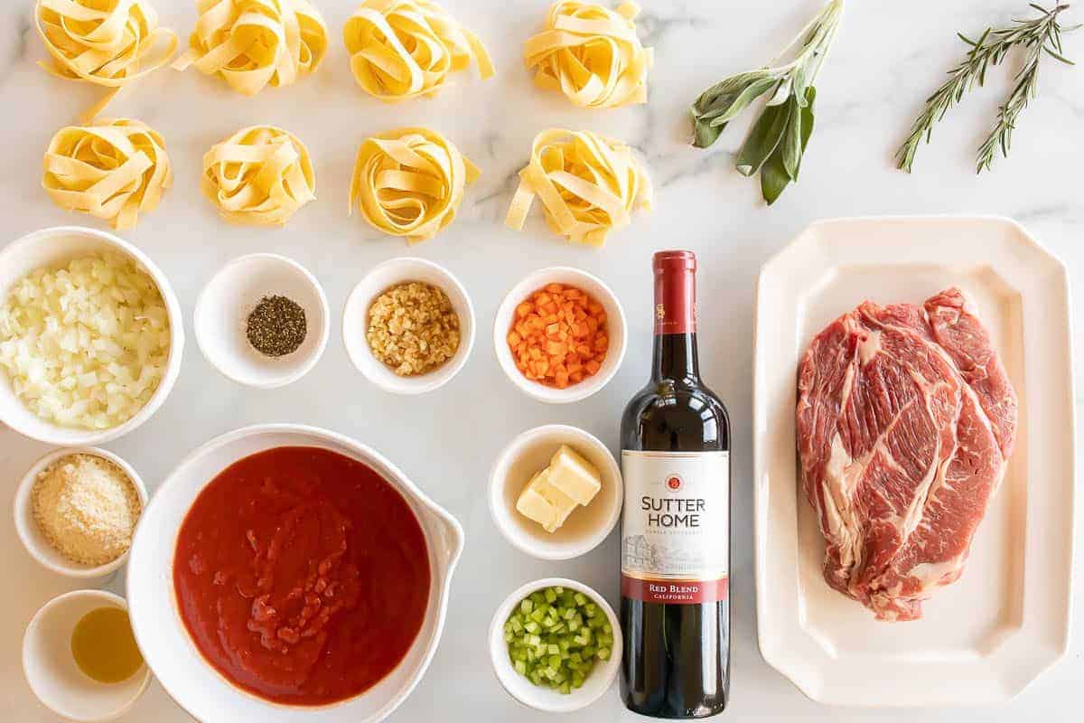 Ingredients for a beef ragu recipe laid out on a white marble surface.