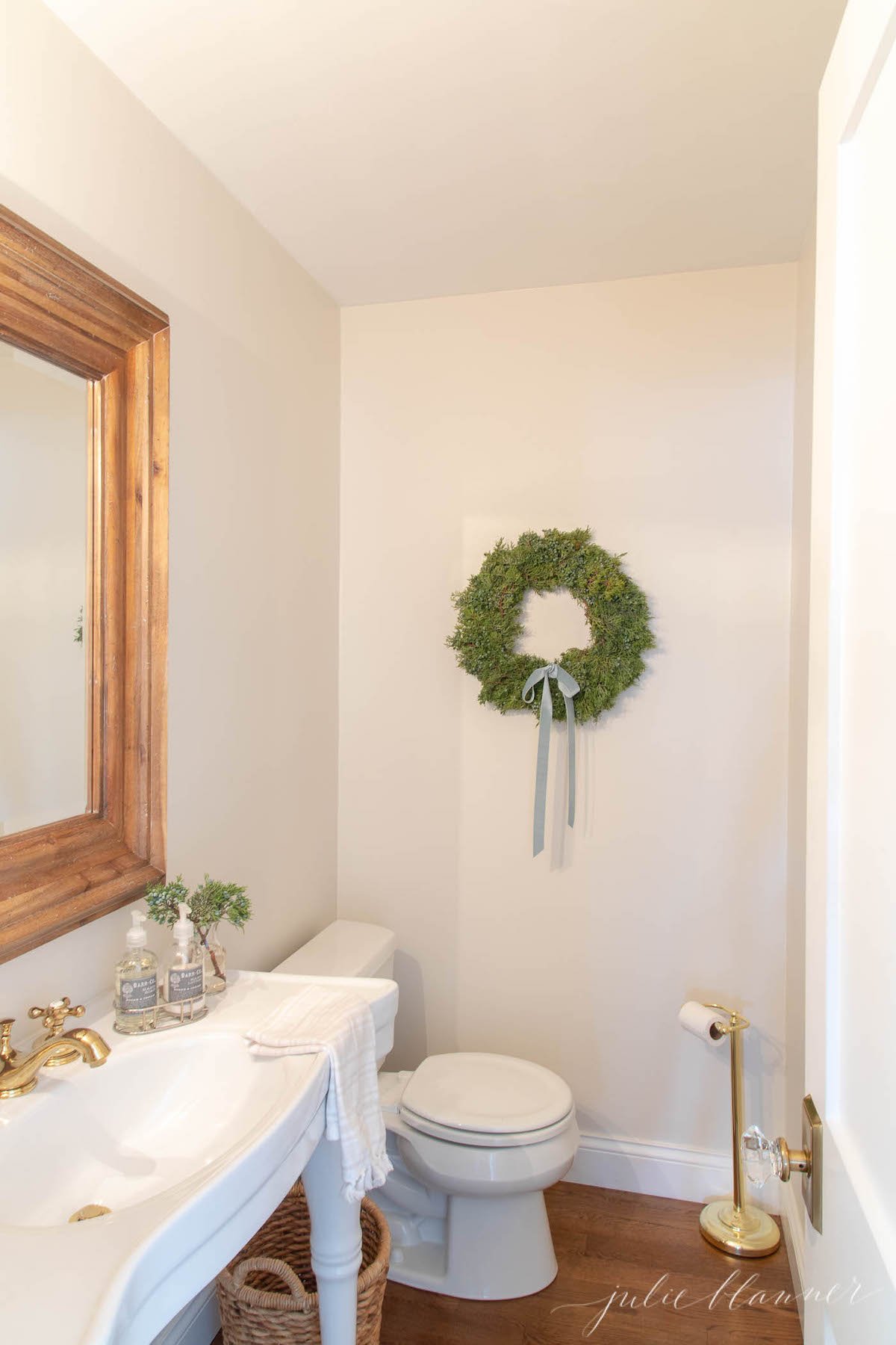 A bathroom with a wreath hanging on the wall adorned with blue Christmas decorations.