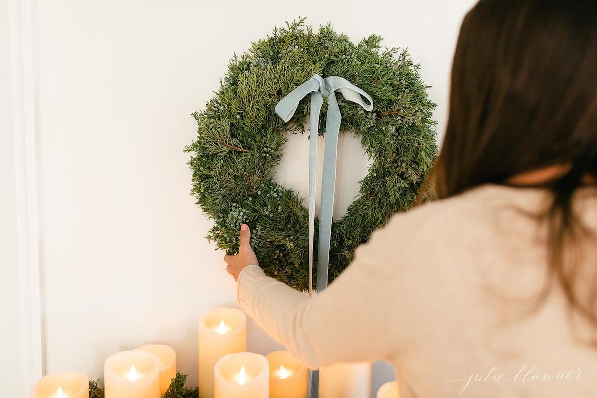 A woman decorating a holiday home with a wreath and candles in blue christmas decorations.