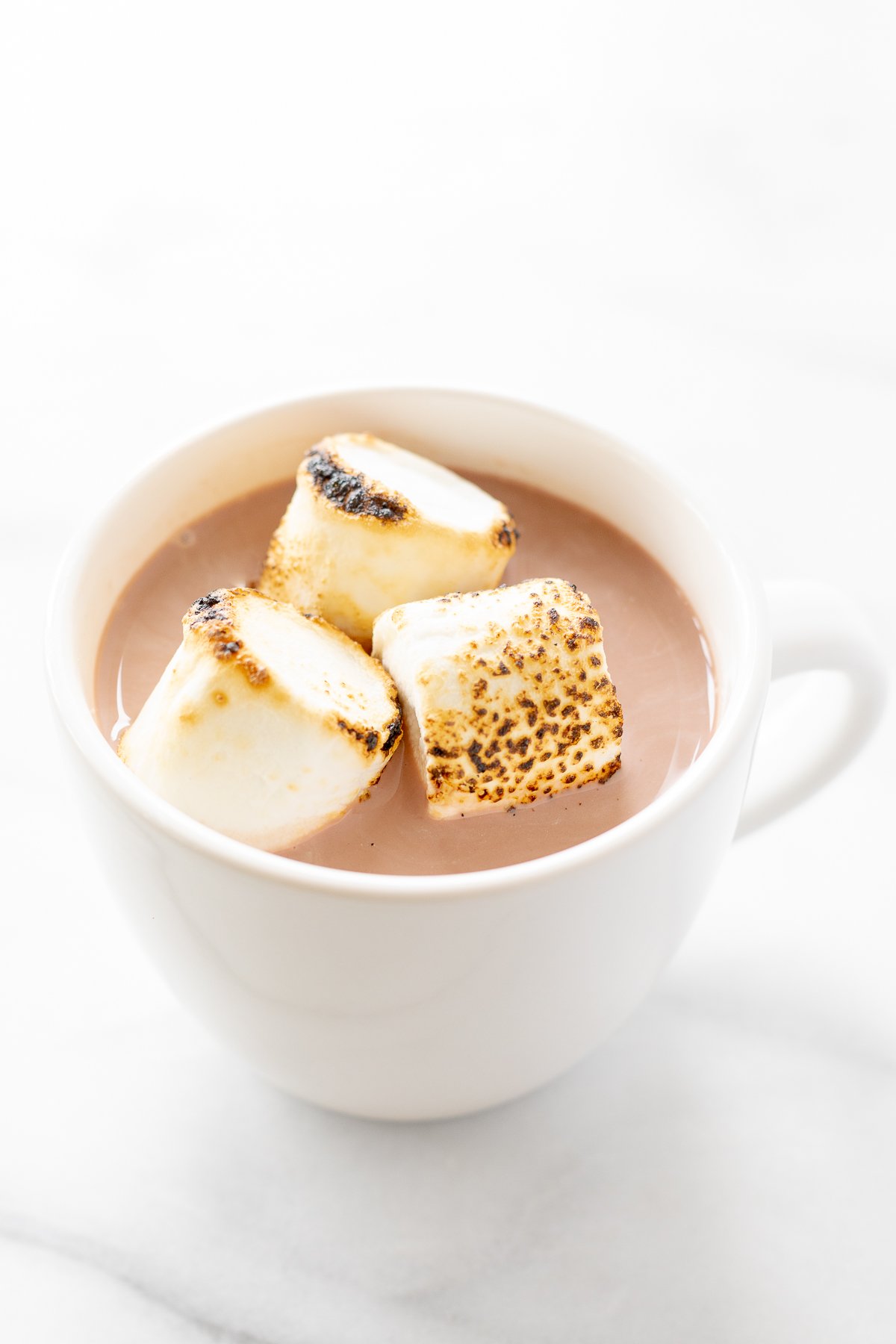 A white mug full of spiked hot chocolate, topped with toasted marshmallows.