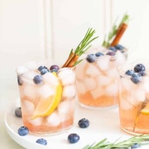 Trio of clear glasses full of a bourbon smash recipe with rosemary and cinnamon stick for garnish.