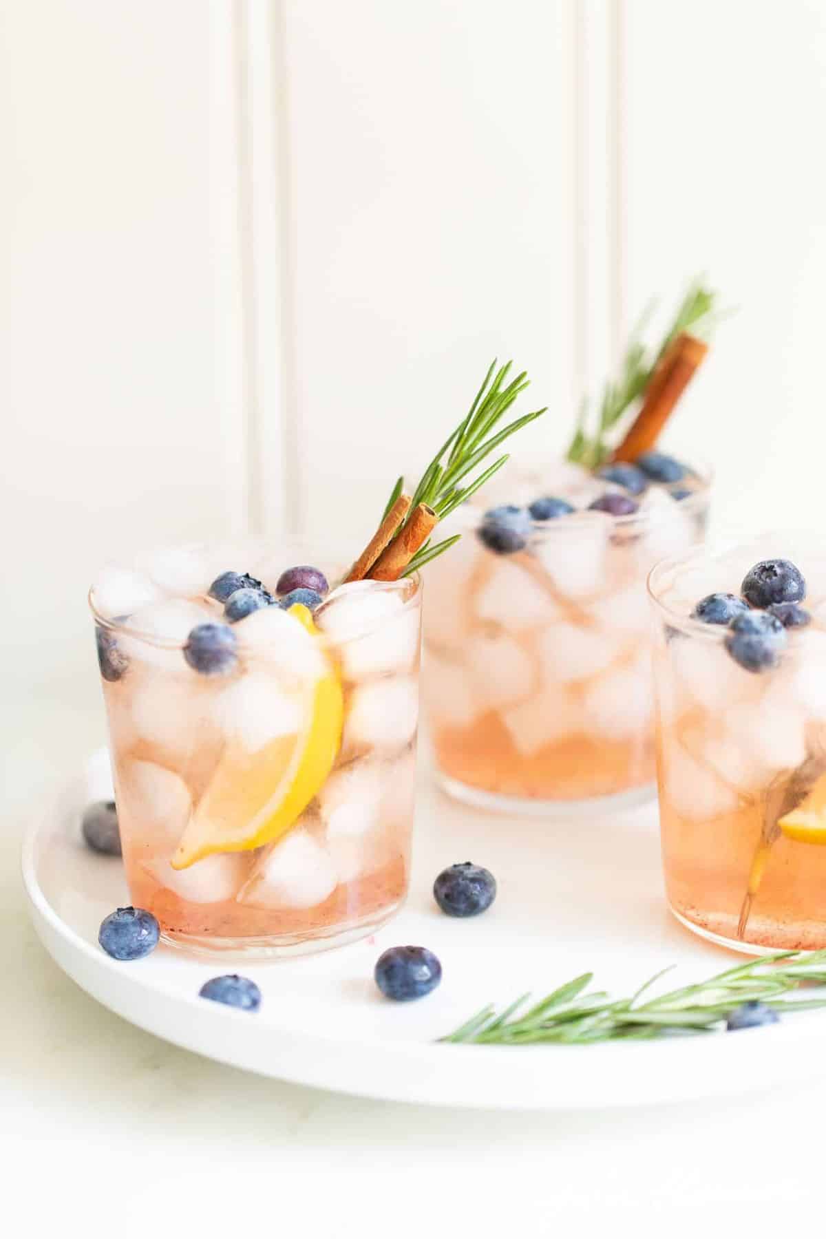 Trio of clear glasses full of a bourbon smash recipe with rosemary and cinnamon stick for garnish.