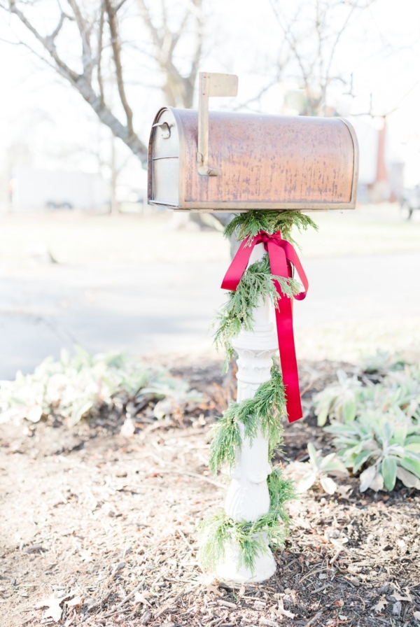 A copper mailbox with Christmas mailbox decorations of a cedar garland and a red bow.