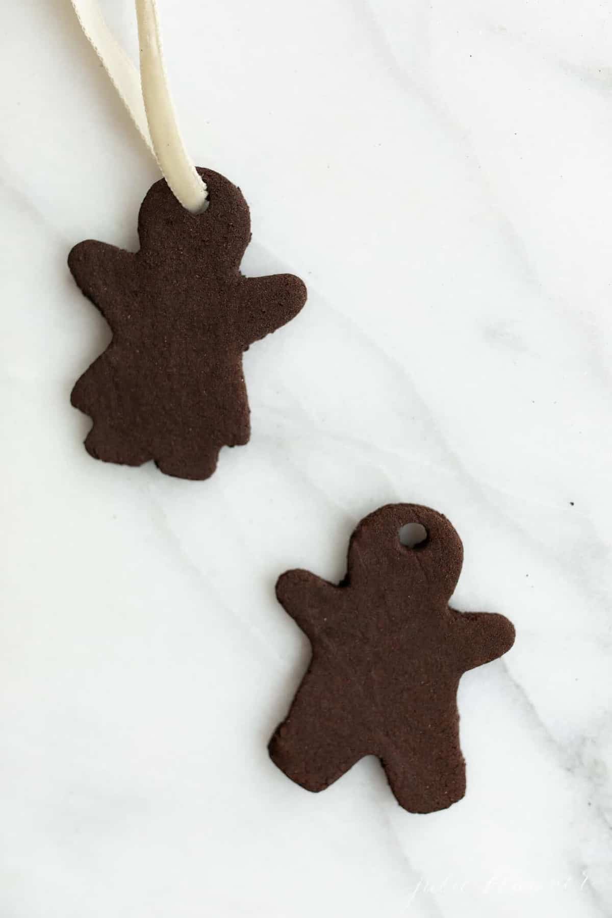 Two gingerbread cutout cinnamon applesauce ornaments on a marble surface.