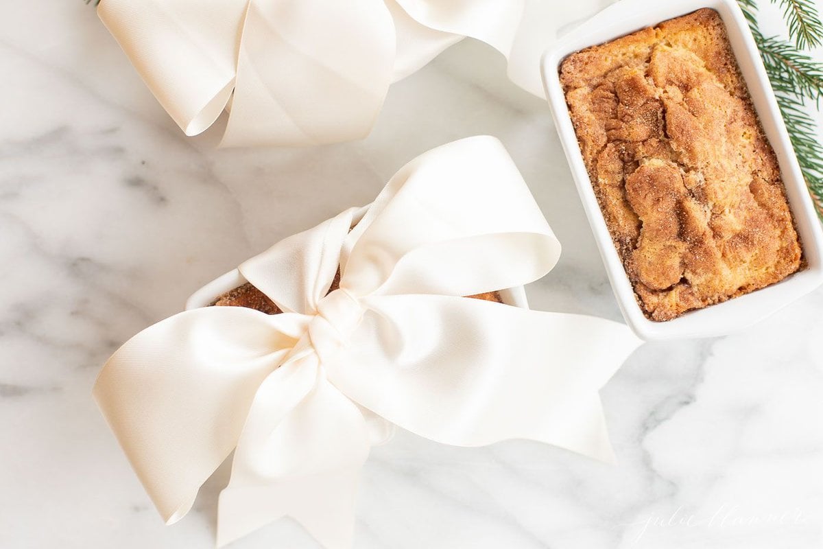 Small loaves of cinnamon bread, tied with ivory ribbon on a marble countertop for a Christmas gift.