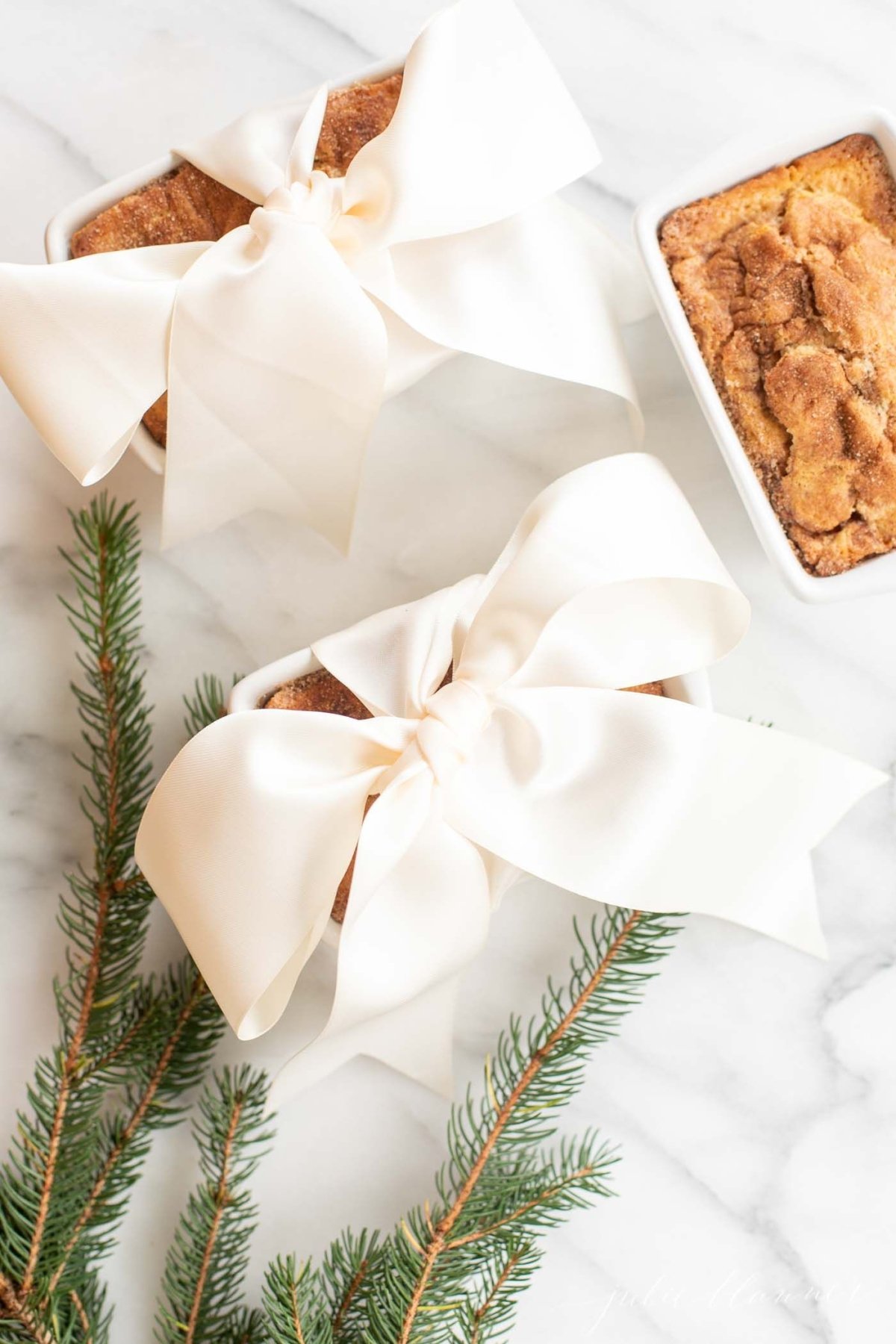 Small loaves of cinnamon bread, tied with ivory ribbon on a marble countertop for a Christmas gift.