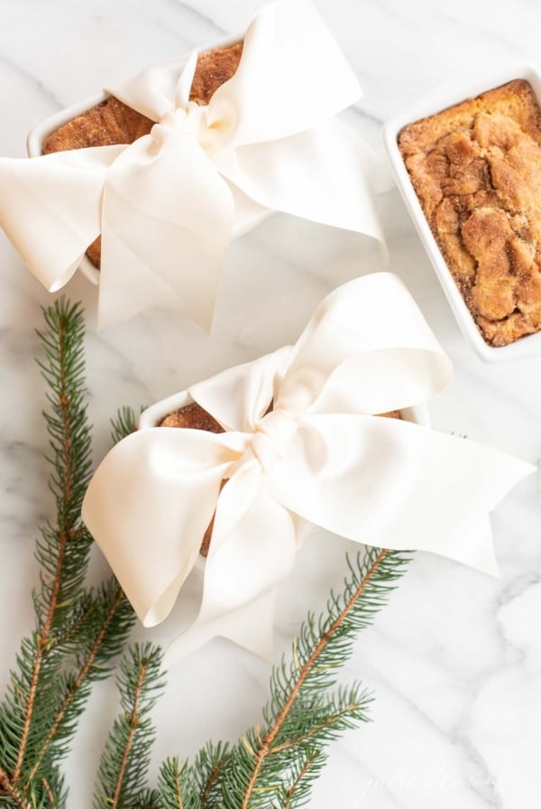 Small loaves of cinnamon bread, tied with ivory ribbon on a marble countertop for a Christmas gift.