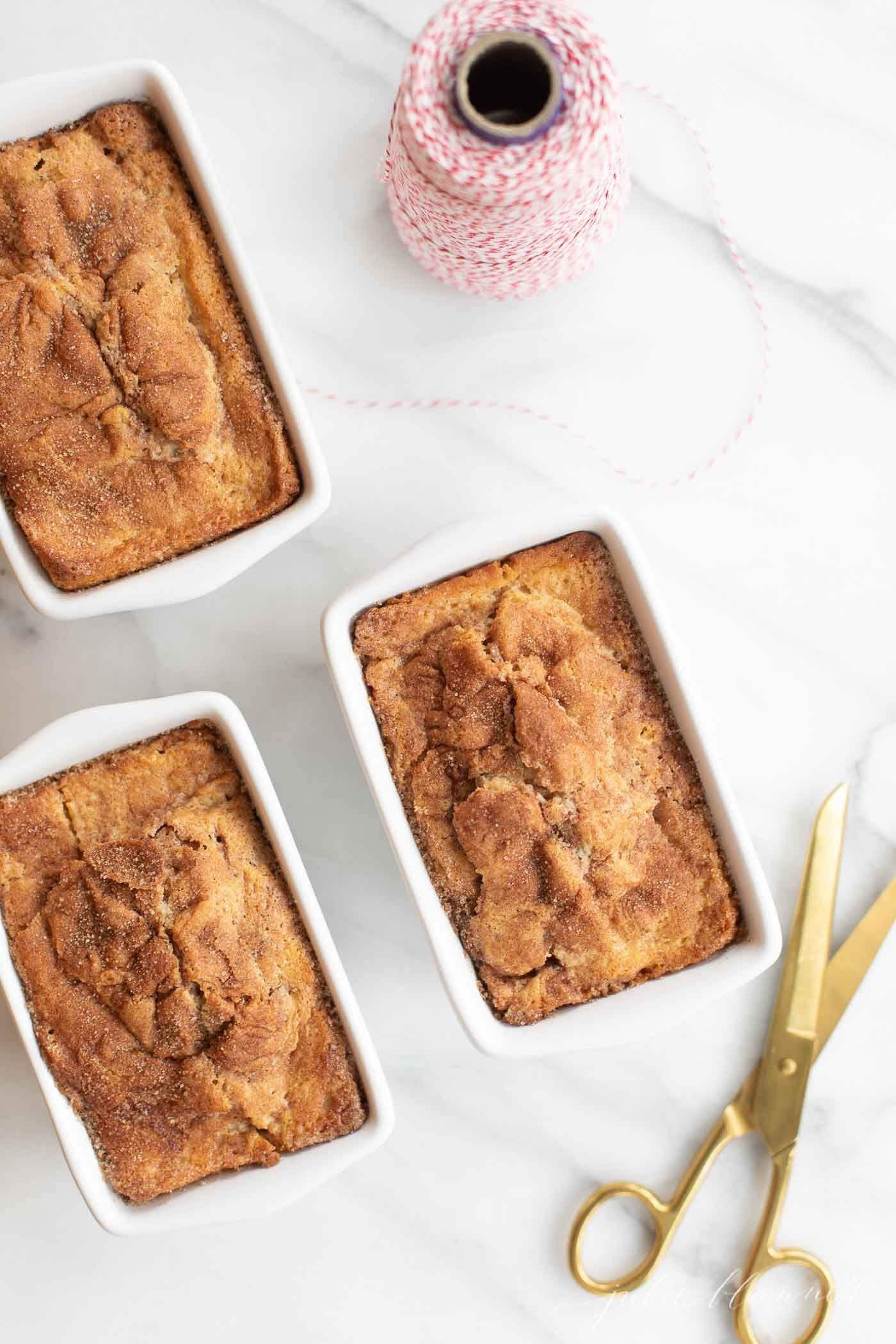 Mini loaves of cinnamon bread on a marble countertop, next to scissors and twine for a gift.