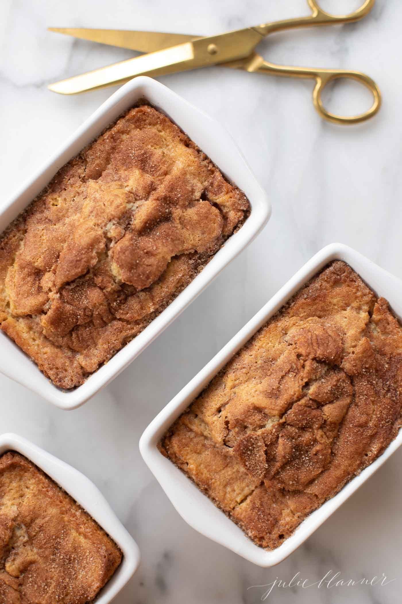 Mini loaves of cinnamon bread on a marble countertop, next to scissors and twine for a gift.