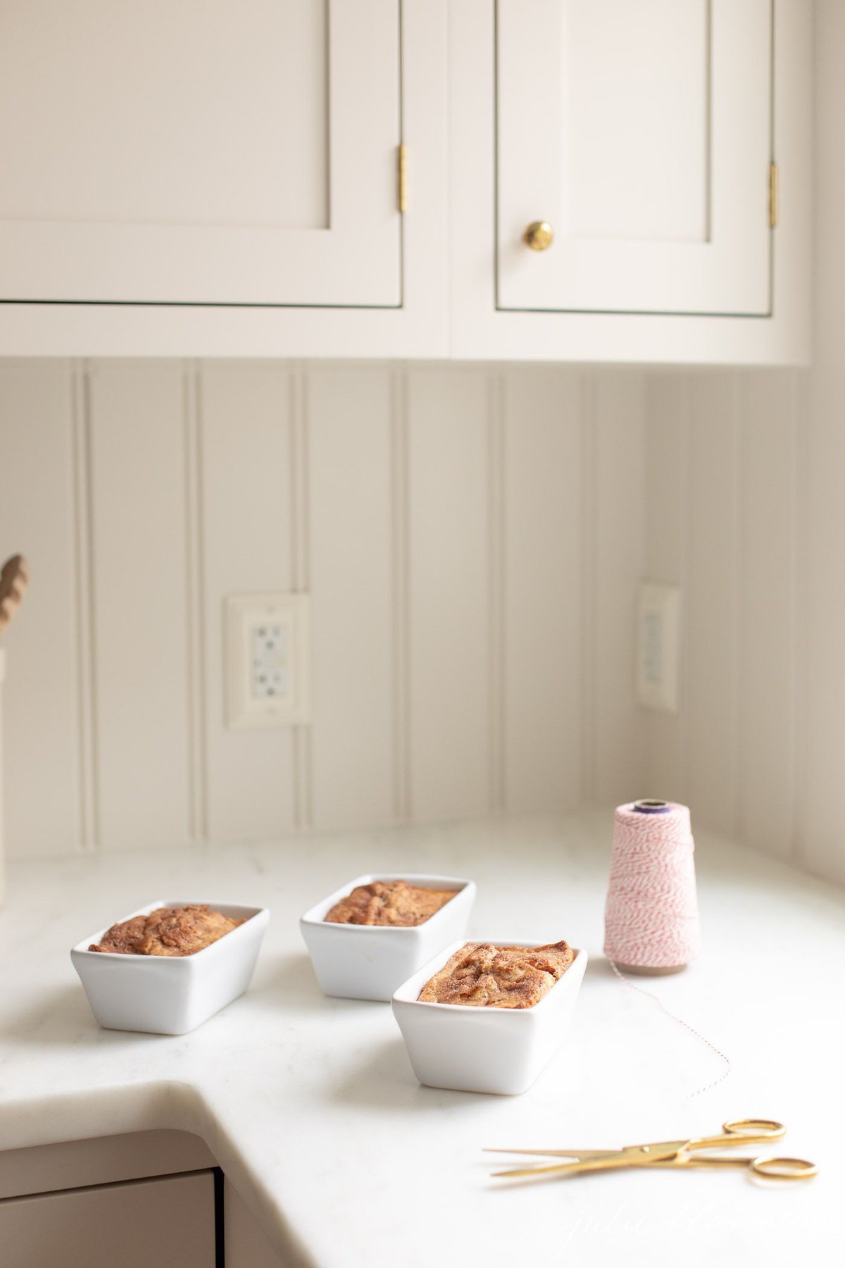 Mini loaves of cinnamon bread on a marble countertop, next to scissors and twine for a gift.