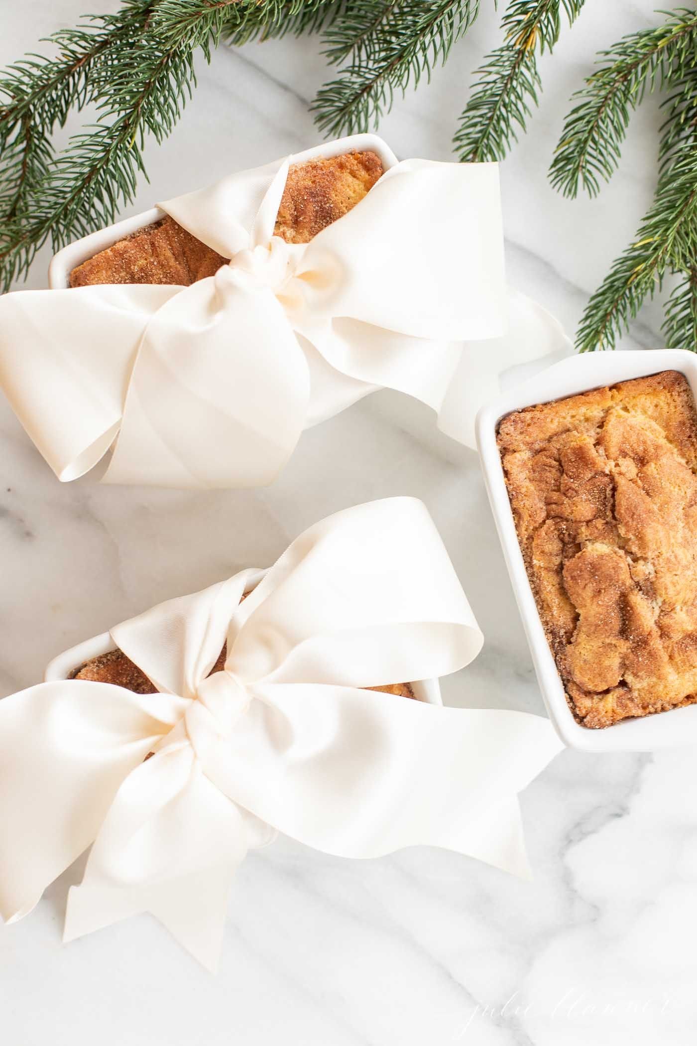 Small loaves of cinnamon bread, tied with ivory ribbon on a marble countertop for a Christmas gift.