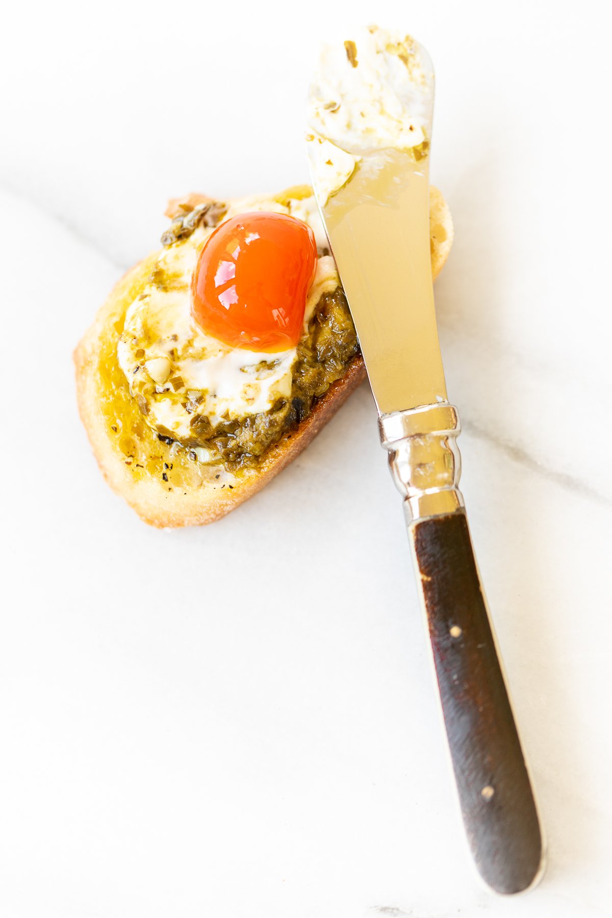 A piece of bread with an egg on it and a pesto cheese dip.