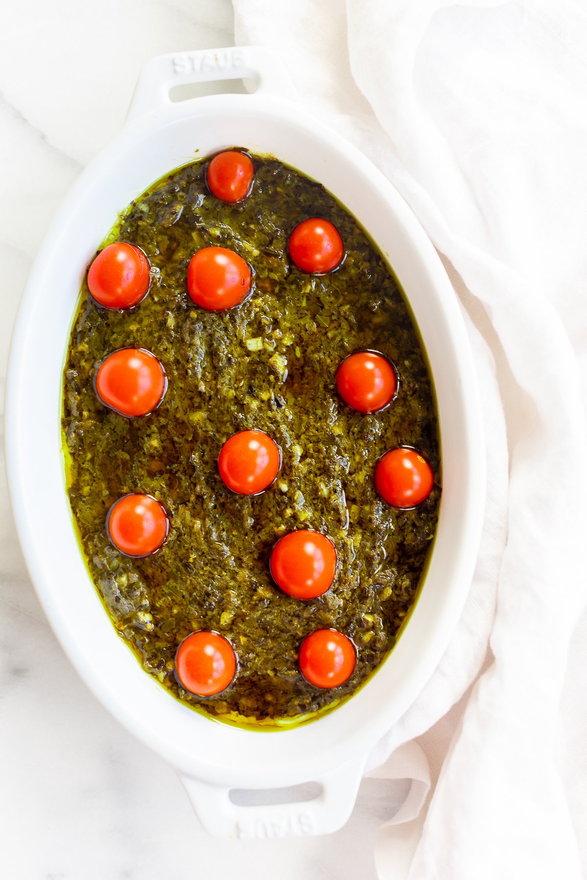 An easy appetizer dip with a white dish filled with pesto and tomatoes.