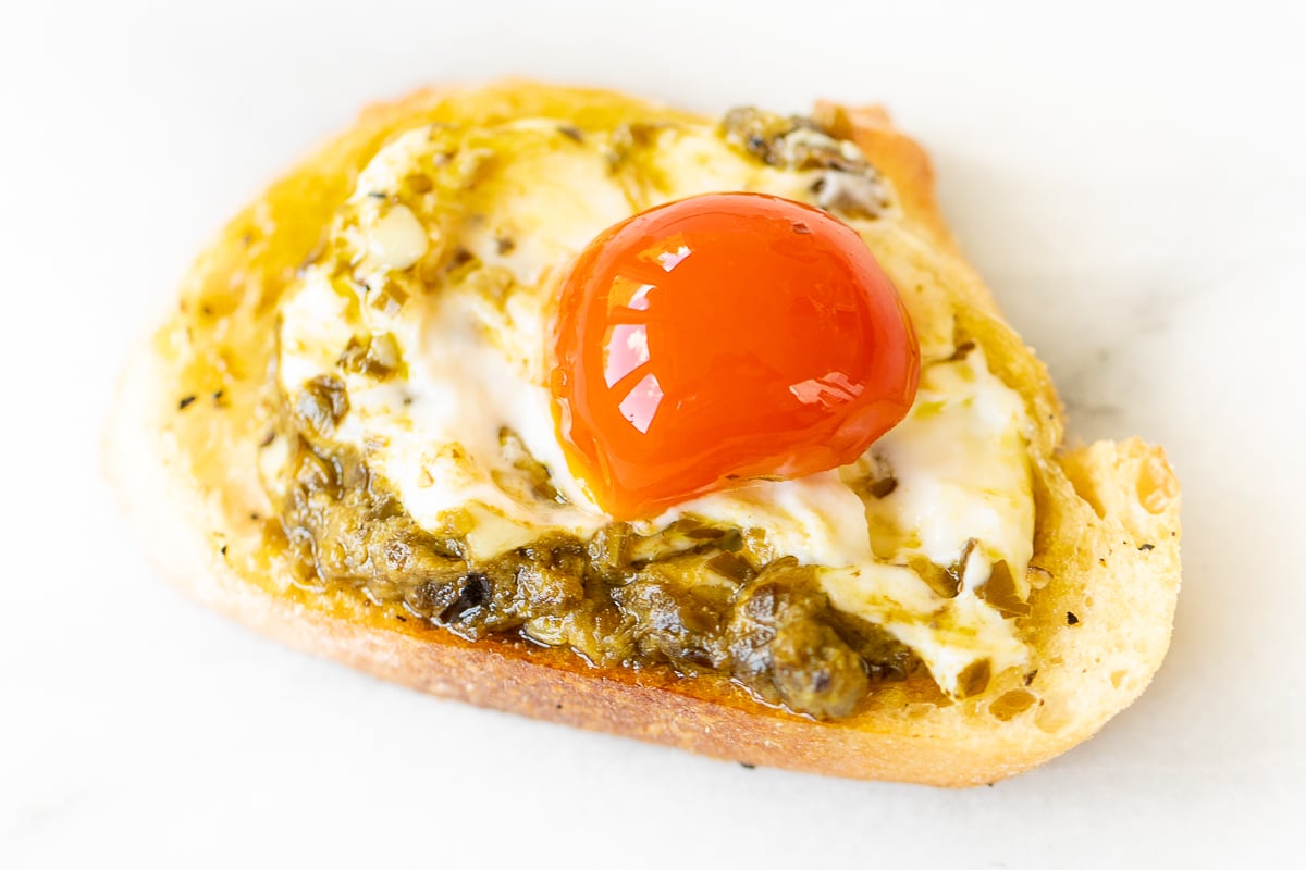 An easy appetizer dip with a pesto cheese spread on a piece of bread with a tomato on top.