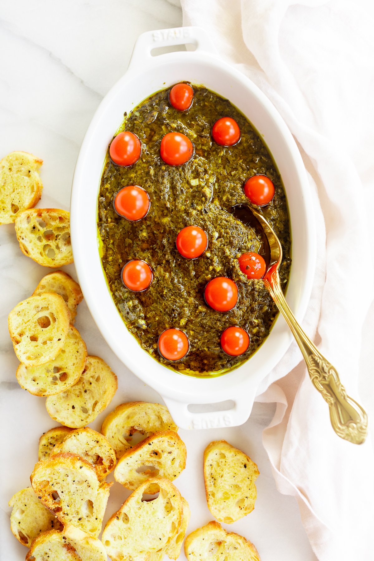 A white bowl of pesto dip with cherry tomatoes and croutons, an easy appetizer dip.