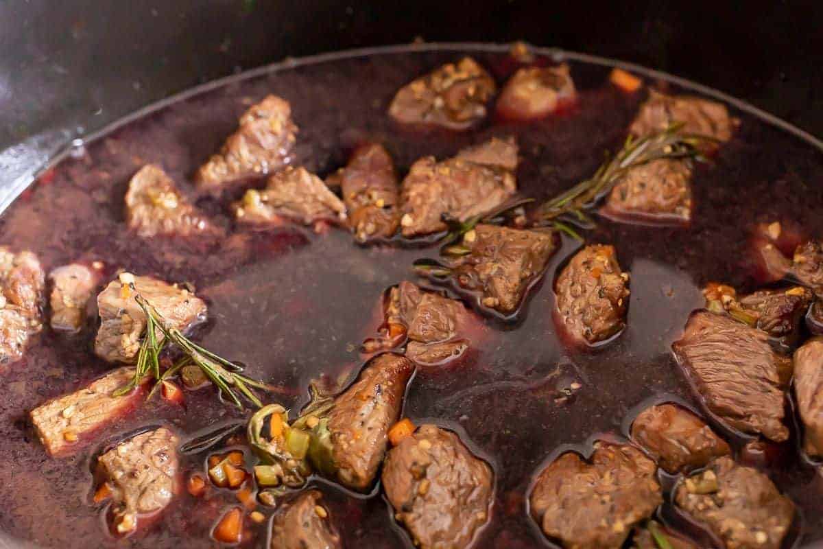 Looking into a steaming cast iron pot filled with beef ragu ingredients.