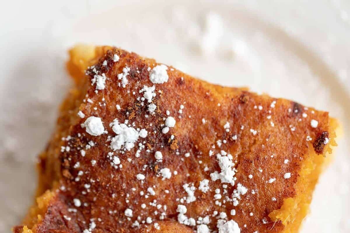 close up of a slice of pumpkin gooey butter cake sprinkled with powder sugar.