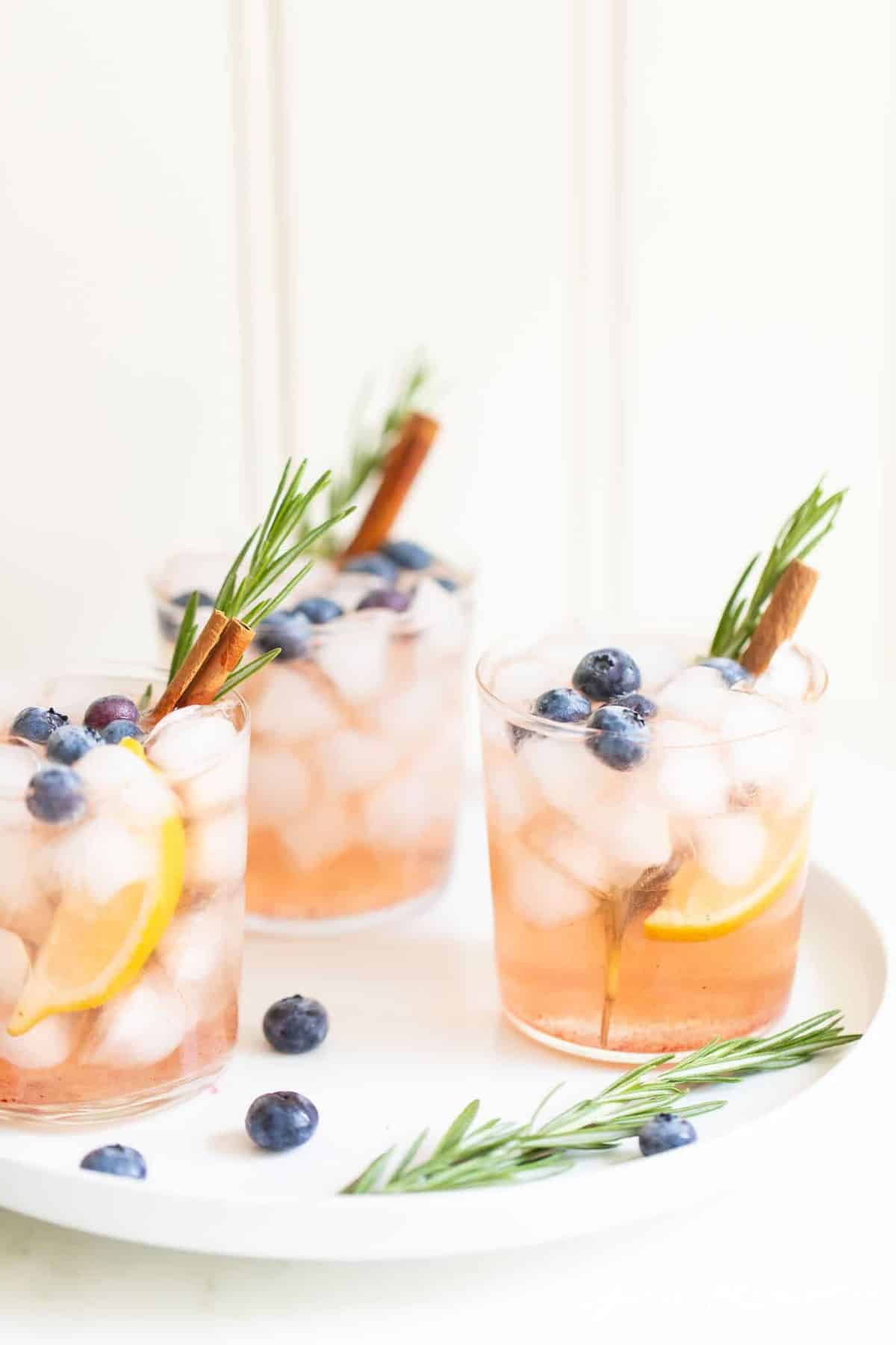 Trio of clear glasses full of a whiskey smash recipe with rosemary and cinnamon stick for garnish.