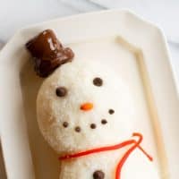 White surface, snowman cheeseball on a platter, chocolate chip smile.