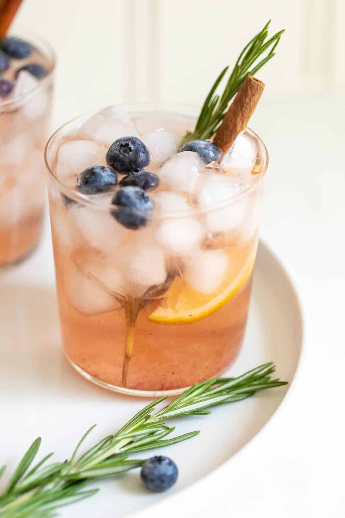 Clear glass of a whiskey smash cocktail recipe, rosemary and cinnamon for garnish.