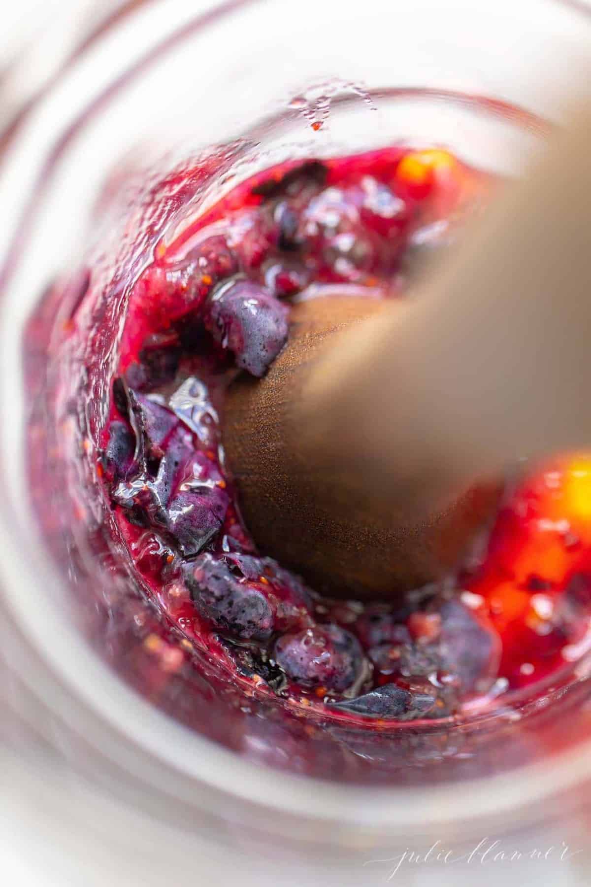 Looking into a pitcher of smashed fruit for a whiskey smash recipe, muddler at work.