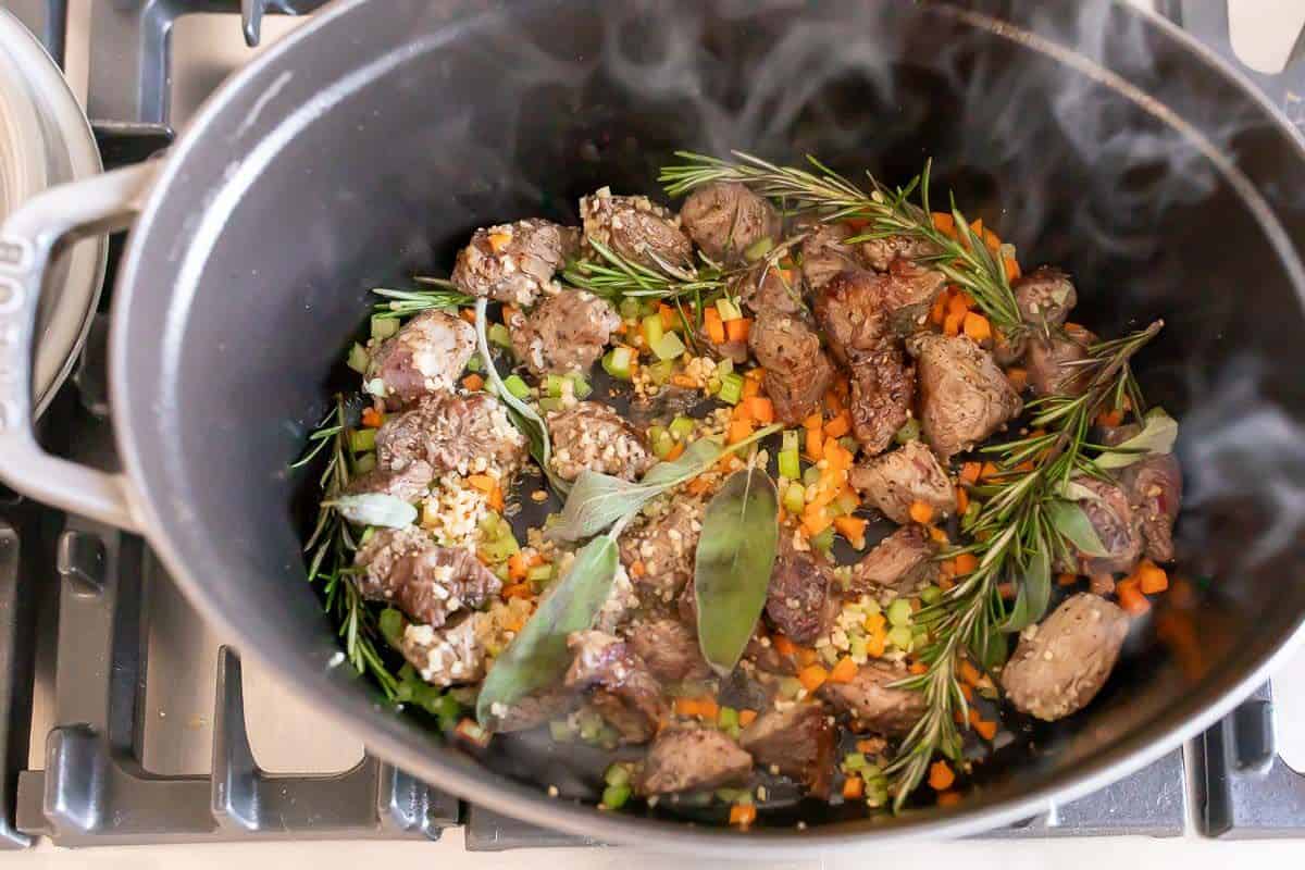 Looking into a steaming cast iron pot filled with beef ragu ingredients.