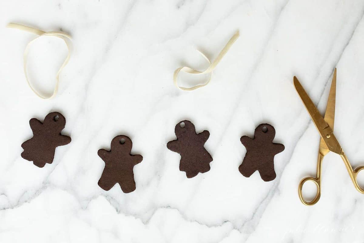 Marble surface, four gingerbread cinnamon ornaments with gold scissors to the side.