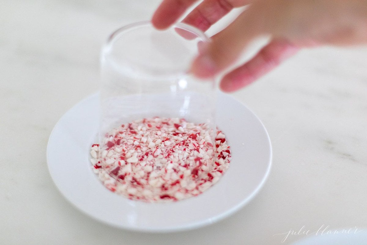 A clear glass being placed upside down onto a plate of crushed peppermint.