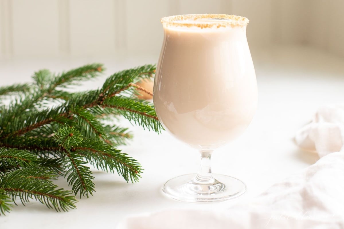 A clear glass with an oatmeal cookie cocktail, fresh winter greens on the edge of the image.