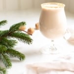 A clear glass with an oatmeal cookie cocktail, fresh winter greens on the edge of the image.