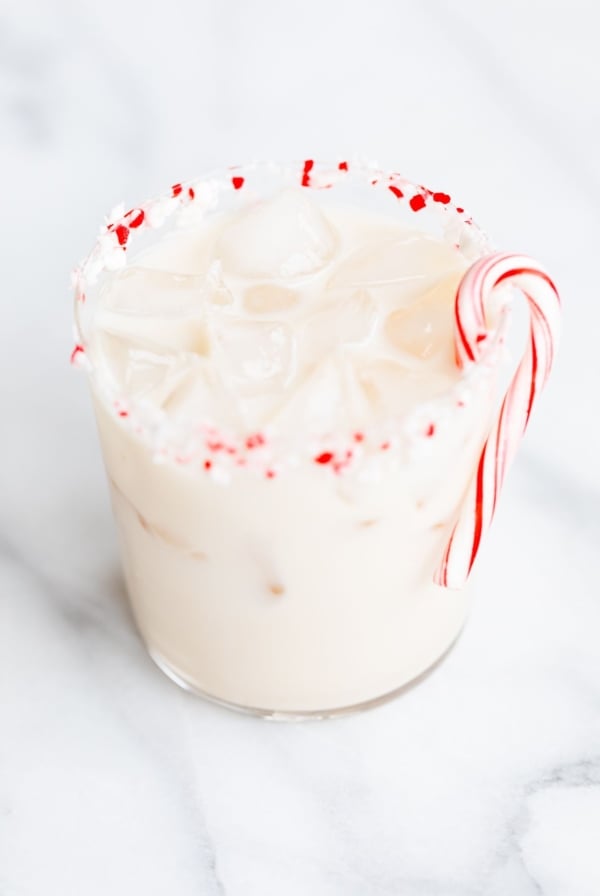 A peppermint white russian cocktail, garnished with a candy cane and crushed peppermint on the rim.