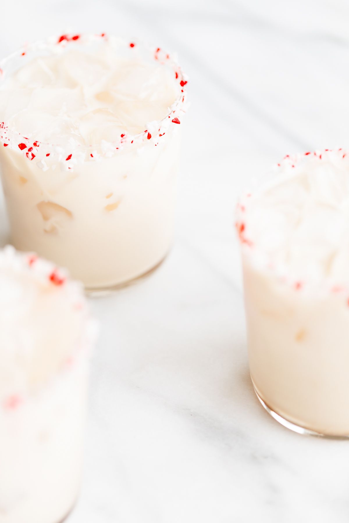 A peppermint white russian cocktail, garnished with a candy cane and crushed peppermint on the rim.